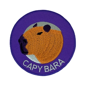May include: A purple and white embroidered patch with a cartoon capybara on a white background. The text "CAPYBARA" is written in white below the capybara.