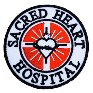 Può includere: Toppa ricamata bianca con bordo nero. Il centro presenta un cuore rosso con una corona di spine e una croce. Il testo "SACRED HEART HOSPITAL" è scritto in un cerchio nero attorno al cuore.