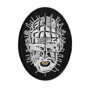 May include: Black and white embroidered patch of a horror movie character's face with a metal head and sharp teeth. The character's eyes are covered with a metal grid.