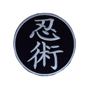 Peut inclure: Un écusson brodé noir et blanc avec les caractères japonais pour "忍術" (Ninjutsu) dans un cercle.