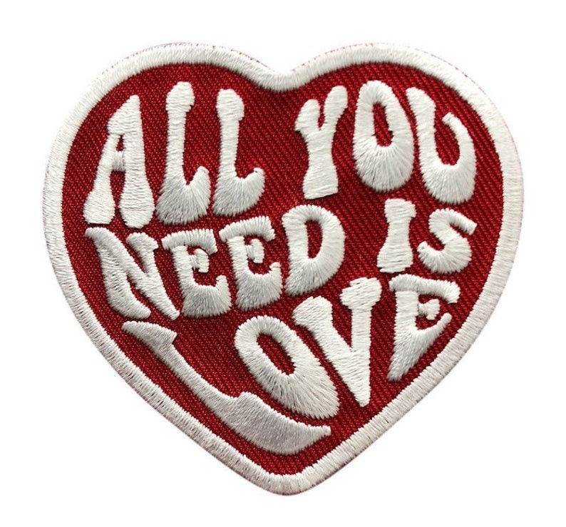 Op de afbeelding: Rode hartvormige patch met witte geborduurde tekst die "All You Need Is Love" luidt.