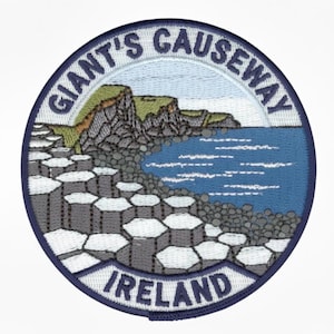 Puede incluir: Parche bordado circular que representa la Calzada de los Gigantes en Irlanda del Norte. El diseño incluye el texto "GIANT'S CAUSEWAY" e "IRELAND" en letras blancas, con un borde azul y un paisaje costero.