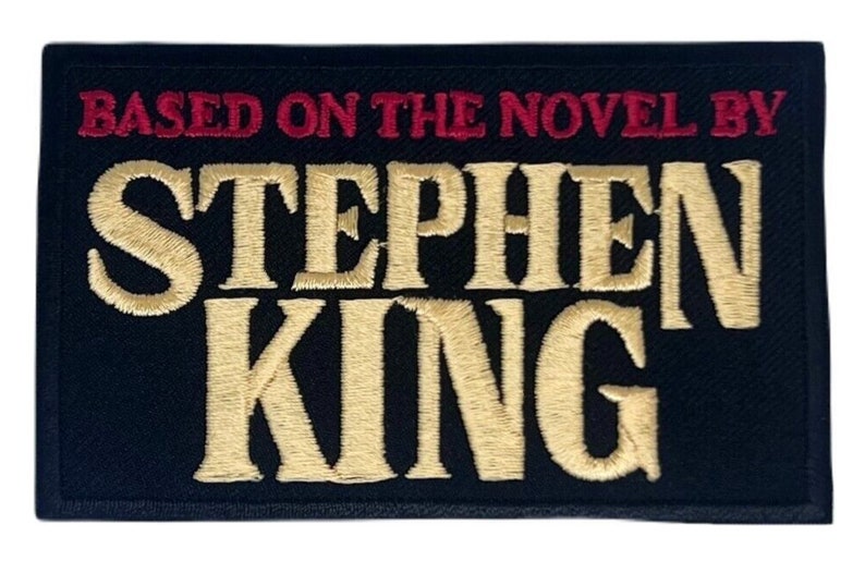 K&ouml;nnte beinhalten: Schwarzer gestickter Aufn&auml;her mit dem Text "Based on the novel by Stephen King" in roter und goldener Farbe.