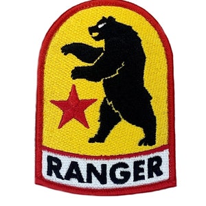 以下が含まれることがあります： 黒熊が後ろ足で立ち、赤い星が描かれた黄色と赤の刺繍パッチ。熊の下に白い文字で「RANGER」と書かれている。