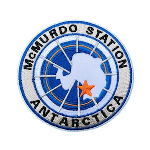 Puede incluir: Parche bordado circular con la inscripción "McMurdo Station Antarctica". El diseño presenta una combinación de colores azul y blanco, una estrella naranja y un contorno blanco de la Antártida.