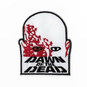 Op de afbeelding: Witte geborduurde patch met een rood zombiegezicht en de tekst "Dawn of the Dead" in zwart.