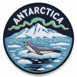 Op de afbeelding: Geborduurde patch met een zeehond die op een ijsberg in Antarctica rust. De patch heeft een marineblauwe rand met het woord "ANTARCTICA" in het wit. Het ontwerp omvat een bergketen, aurora borealis en ijsschotsen in blauwe, witte en groene tinten.
