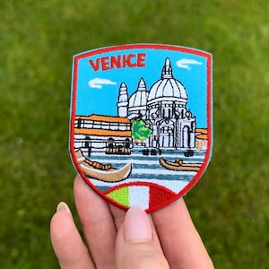 Op de afbeelding: Geborduurde patch met een schildvorm met het woord "VENICE" bovenaan. De patch toont een Venetiaanse scène met gondels, gebouwen en een blauwe lucht. De onderkant van de patch heeft de kleuren van de Italiaanse vlag.