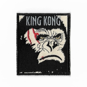 Op de afbeelding: Een geborduurde patch in zwart en wit met de woorden "KING KONG" in zilverdraad. De patch toont een close-up van King Kongs gezicht met een rood litteken.