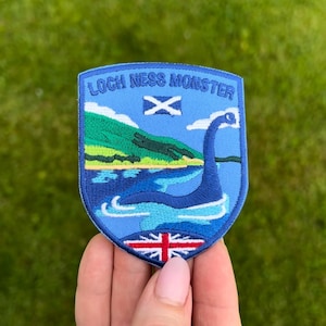 May include: A blue and green embroidered patch with the text "Loch Ness Monster" and a depiction of the Loch Ness Monster in the water. The patch also features the flags of Scotland and the United Kingdom.