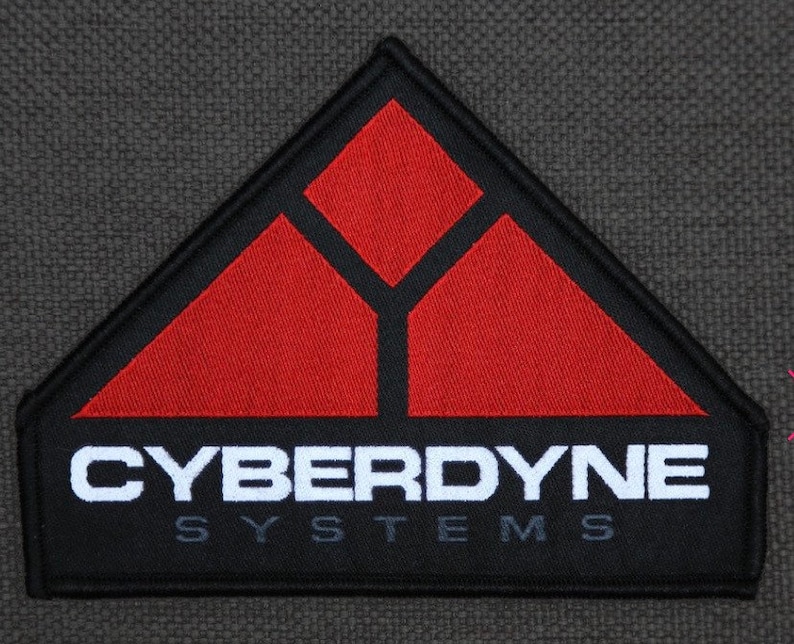 May include: A black and red embroidered patch with the text "CYBERDYNE SYSTEMS" in white. The patch features a stylized triangle with three smaller triangles inside.