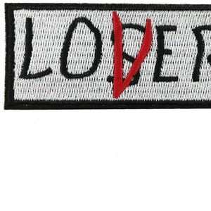 Op de afbeelding: Zwarte en witte geborduurde patch met het woord "LOSER" in zwart en een rode streep door de "O".