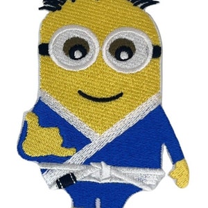 Op de afbeelding: Een geel minion-cartoonfiguur dat een blauw martial arts-uniform draagt met een witte band. De minion glimlacht en geeft een duim omhoog.