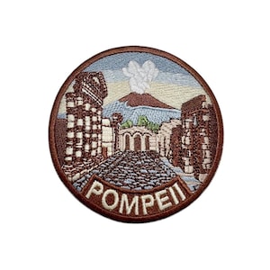 Op de afbeelding: Ronde geborduurde patch met een afbeelding van Pompeii, Italië. Het ontwerp toont oude ruïnes, een geplaveide straat en een vulkaan met een rookpluim. Het woord "POMPEII" is geborduurd op een gebogen banner. De patch heeft een bruine rand.