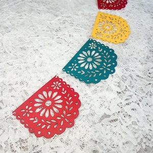 May include: A decorative garland featuring a series of semi-circular paper cutouts in red, yellow, and teal. Each piece displays an intricate, symmetrical floral pattern with scalloped edges, all strung together on a thin white cord.