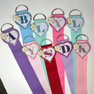May include: Nine colourful ribbon hangers with heart-shaped embellishments featuring letters A, Y, S, D, K, L, X, B, and a flower design.
