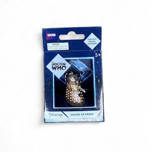 Puede incluir: Un llavero Dalek de metal fundido de la serie Doctor Who, presentado en una caja azul. La caja presenta el logotipo de la BBC, el logotipo de Doctor Who y una advertencia sobre piezas pequeñas. Apto para mayores de 5 años.