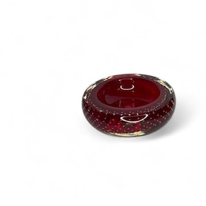 Può includere: Una piccola ciotola rotonda in vetro rosso rubino con una texture a bolle. La ciotola ha un interno liscio e lucido e un esterno leggermente strutturato. Il bordo è di una tonalità più chiara di rosso, su sfondo bianco.