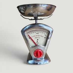 May include: A vintage chrome and red Dutton kitchen scale. The scale features a round bowl, a dial with a red needle, and a red knob. The dial reads up to 1 kg and includes the text "NOT LEGAL FOR USE IN TRADE".