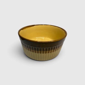 May include: A round ceramic bowl featuring a two-tone design with a cream-colored interior and a dark brown upper exterior rim. The lower exterior of the bowl is cream-colored and features a vertical ribbed texture around the entire circumference.