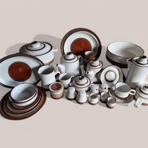 May include: A large collection of ceramic dinnerware featuring a cream-coloured base with dark brown circular accents and rim detailing. The set includes various plates, bowls, teapots, a lidded casserole dish, a creamer, a sugar bowl, and cups.