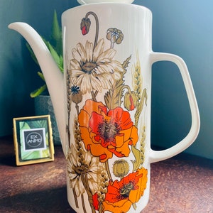 May include: White ceramic coffee pot with a floral design featuring orange poppies, white daisies, and wheat stalks. The pot has a lid and a handle.