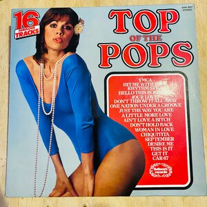 May include: A vintage vinyl record album cover for "Top of the Pops" featuring a woman in a blue bodysuit. The album cover has the text "16 Fabulous Tracks" and a list of song titles. The Hallmark Records logo is visible.