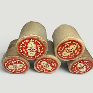 May include: A collection of six spools of thread wrapped in tan paper. Each spool has a red and white label with the text "3 Cord No. 60 2 Ounce". The spools are arranged in a slightly overlapping pattern.