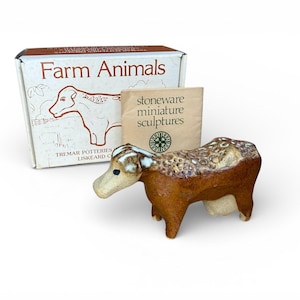 May include: A ceramic cow figurine in shades of brown and cream. The cow is part of a set of stoneware miniature sculptures. The box reads "Farm Animals" and "Tremar Potteries Liskeard Cornwall".