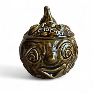 May include: A green ceramic chutney jar shaped like a face with a wide smile and large eyes. The lid is shaped like an onion and has the word "CHUTNEY" written on it.