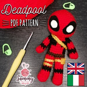 Può includere: Bambola amigurumi Deadpool realizzata a uncinetto in rosso, nero e oro. La bambola indossa un costume rosso e nero con una cintura dorata e una maschera nera per gli occhi. La bambola è in piedi su una superficie di legno. L'immagine include anche un uncinetto, dei marcatori di punti e il testo "Deadpool = PDF PATTERN = ".