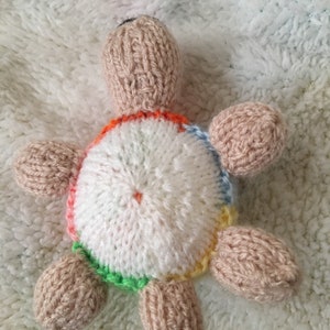 May include: A knitted turtle toy with a white shell and colorful accents. The turtle has a brown body and a black nose.