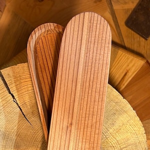 May include: Two wooden serving trays with a light brown finish and vertical grooves. The trays are placed on a wooden surface with a natural wood grain pattern. The trays have a curved, rounded shape.