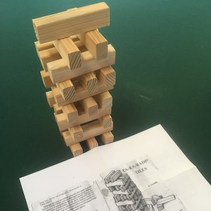 Könnte beinhalten: Eine Nahaufnahme eines Holzspiels namens "Ta-Ka-Radi Tiles". Das Spiel besteht aus Holzblöcken, die übereinander gestapelt werden. Das Spiel wird gespielt, indem man einen Block nach dem anderen entfernt und auf den Stapel legt. Das Spiel ist vorbei, wenn der Turm einstürzt.