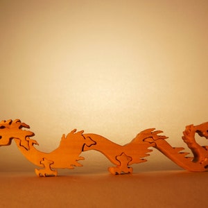 May include: A wooden puzzle of a dragon, with a light brown color. The dragon is curled up in a serpentine shape, with its head raised and its tail curled around its body.