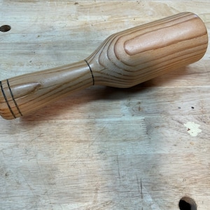 May include: A wooden mallet with a light brown finish and a dark brown handle. The handle has two dark brown bands around it.