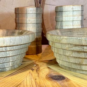 Puede incluir: Tres cuencos de madera con un patrón de veta de madera gris claro y marrón. Los cuencos están apilados uno encima del otro y tienen una forma redondeada. Los cuencos están sobre una superficie de madera.