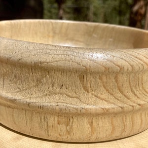 以下が含まれることがあります： 明るい茶色の木製のボウルで、滑らかで磨かれた仕上げになっています。ボウルは広く丸みを帯びた縁と、深く丸みを帯びた内側を持っています。木目の模様はボウル全体に見られます。