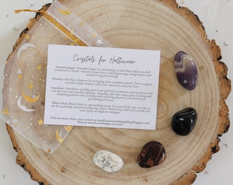 May include: A set of five crystals for Halloween, including amethyst, black onyx, howlite, red jasper, and aurora jasper. The crystals are arranged on a wooden slice with a card that reads "Crystals for Halloween" and describes the properties of each crystal.