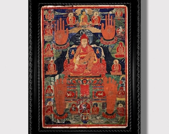May include: A framed religious artwork featuring a central figure in red robes, surrounded by smaller figures and symbols. The artwork has a detailed, colorful design with a blue and green background. The frame is black.
