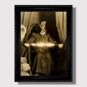 Puede incluir: Una fotografía vintage en sepia de una persona joven sentada en una silla, sosteniendo una cuerda que brilla con luz. La persona lleva un vestido oscuro y un sombrero. La foto está enmarcada en un marco negro.