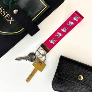 May include: Pink key chain with a silver key ring and two keys. The key chain has a repeating pattern of black and white Australian Shepherd dogs.