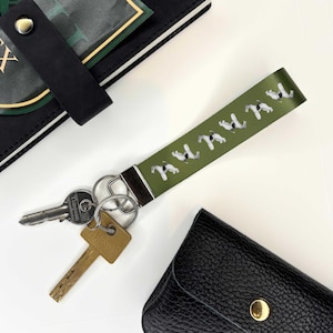 May include: Green key chain with a white dog design and the word "HUMAN" printed on it. The key chain is attached to a set of keys.
