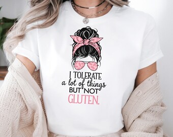 May include: White t-shirt with a graphic of a woman with a pink and black headband and sunglasses. The text "I tolerate a lot of things but not gluten." is printed below the graphic.