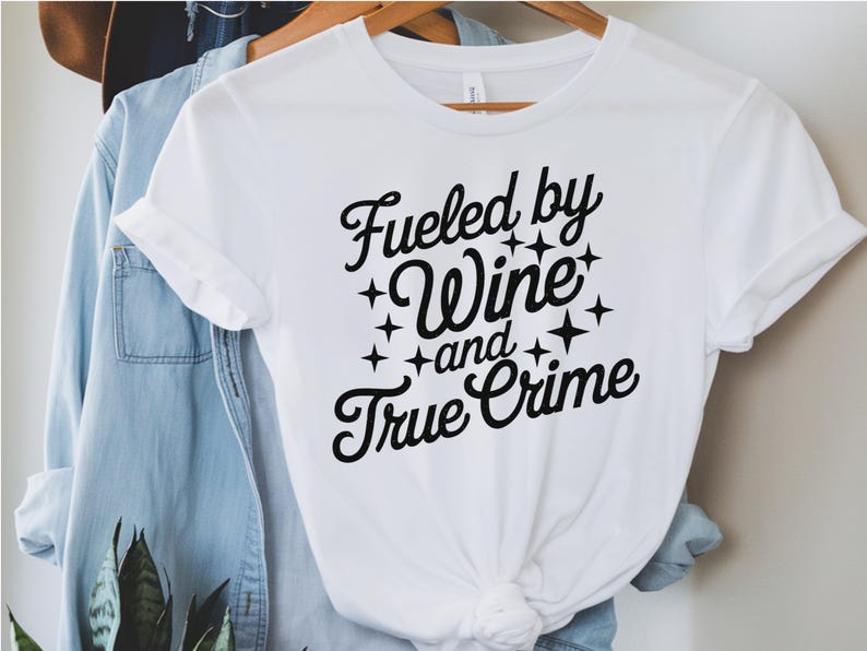 May include: White t-shirt with black text that reads "Fueled by Wine and True Crime" with stars around the text.