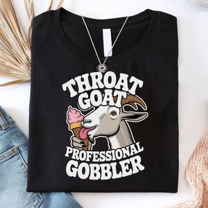 May include: Black t-shirt with a white graphic of a goat eating ice cream. The text "Throat Goat Professional Gobbler" is printed on the shirt.