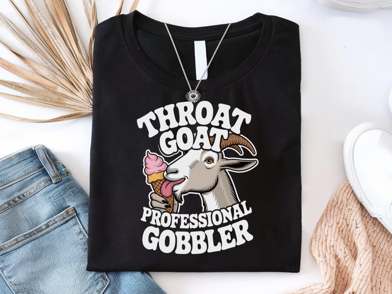 May include: Black t-shirt with a white graphic of a goat eating ice cream. The text "Throat Goat Professional Gobbler" is printed on the shirt.