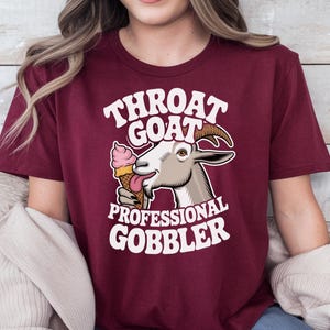 May include: A maroon t-shirt with a white graphic of a goat eating an ice cream cone. The text on the shirt reads "Throat Goat Professional Gobbler".