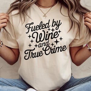 May include: A white t-shirt with black text that reads "Fueled by Wine and True Crime".
