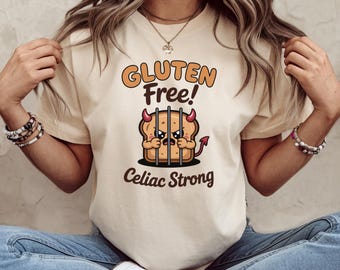 May include: Beige t-shirt with the words "Gluten Free!" in orange lettering above a cartoon slice of bread with devil horns and a tail, behind bars. The text "Celiac Strong" is below the image.